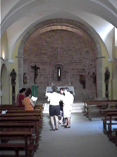Interior de la Iglesia, abside con ventana al fondo; mientras, el coro del pueblo ensaya para las fiestas de San Bartolomé.